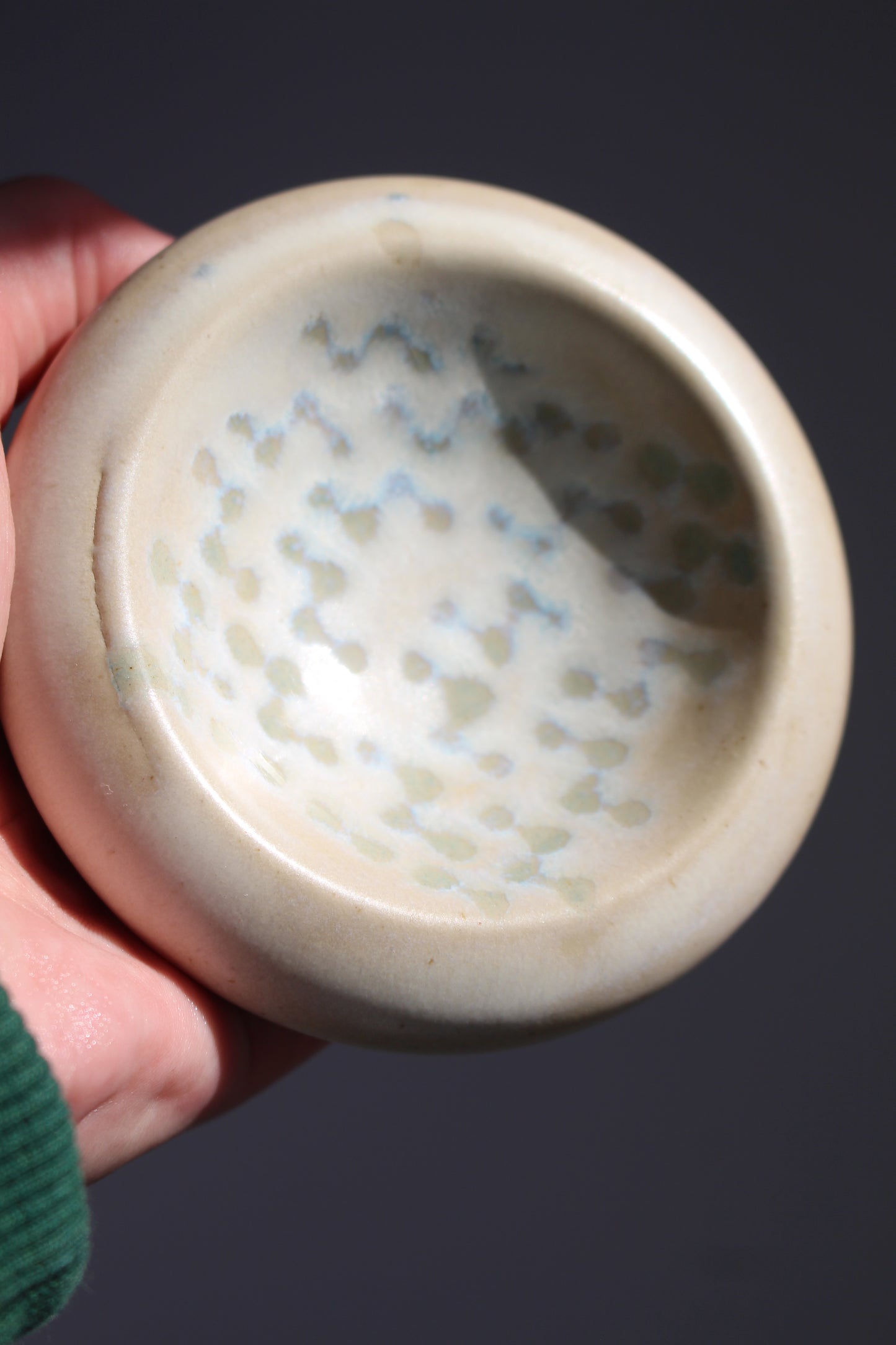 Hand holding a small ceramic bowl with a textured interior against a dark background