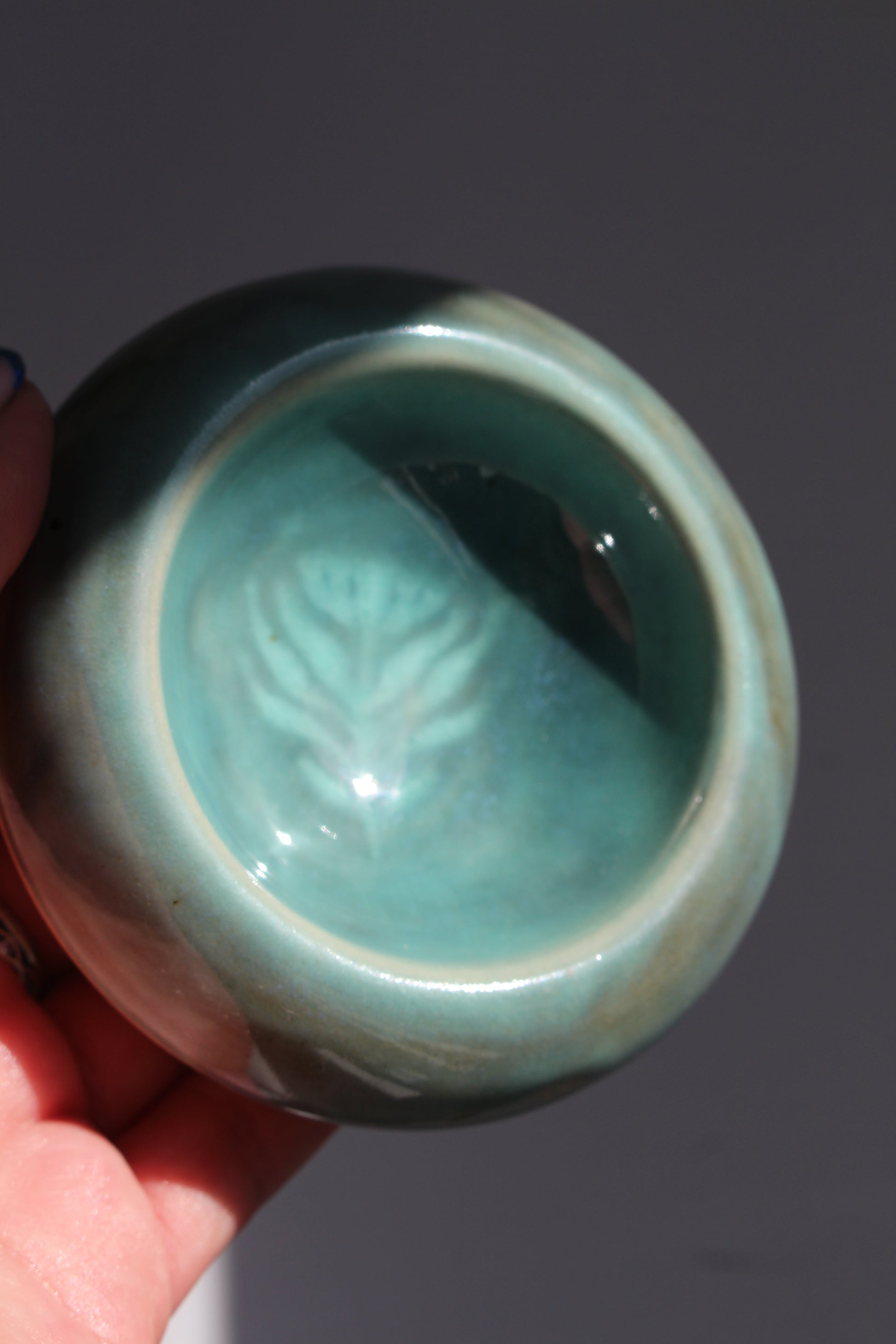 Turquoise ceramic bowl held by a hand against a dark background